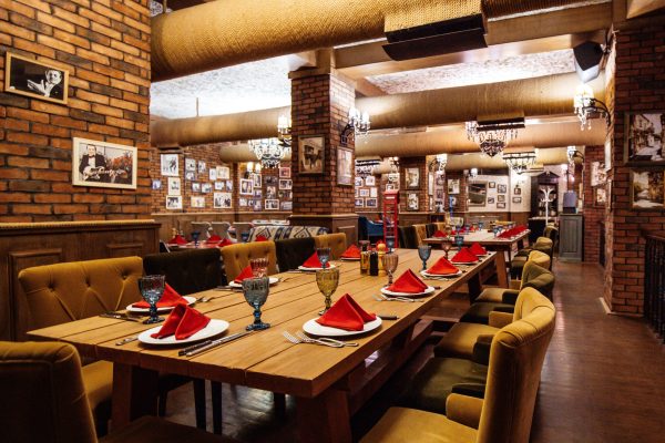 a restaurant hall with red brick walls wooden tables and pipes in the ceiling